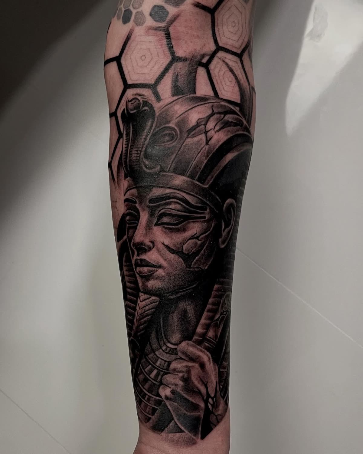 Antebrazo en negro y gris: busto de faraón egipcio con panal geométrico arriba